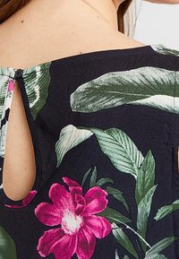 Abito floreale con uno sfondo blu navy e grandi foglie verdi e fiori rosa. Dettaglio con apertura a chiave sulla schiena e chiusura con bottone. Tessuto leggero.
