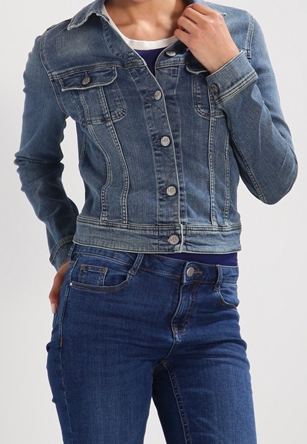 Denimjacka i medelblått, med långa ärmar, knäppning fram, två bröstfickor och en kortad hem. Bärs över en mörkblå topp och jeans.