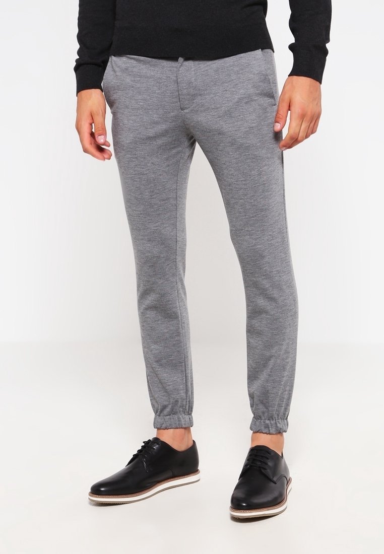 Grå sweatpants med elastiska muddar, tillverkade av mjukt tyg, ihop med svarta läderskor med vita sulor.