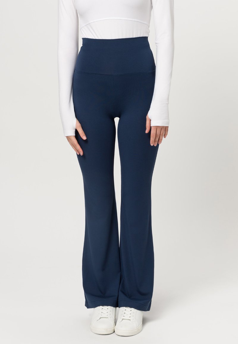 Pantalones acampanados de talle alto en color azul marino, confeccionados en una tela elástica, con una textura suave y una silueta ajustada, combinados con zapatillas deportivas blancas.