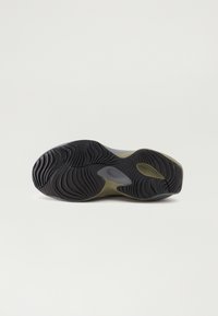 Sålen af en sneaker med en struktureret sort gummioverflade, der har riller og en olivengrøn accent. Den buede form forbedrer grebet.