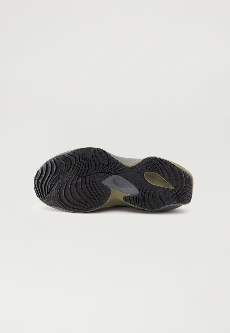Semelle d'une chaussure de sport avec une surface en caoutchouc noir texturé, dotée de rainures et d'une touche de vert olive. Sa forme courbée améliore l'adhérence.