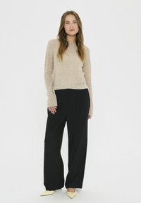 Ljust beige stickad tröja med långa ärmar, kombinerad med svarta vida byxor och spetsiga gula klackar. Enkel textur och rena linjer.