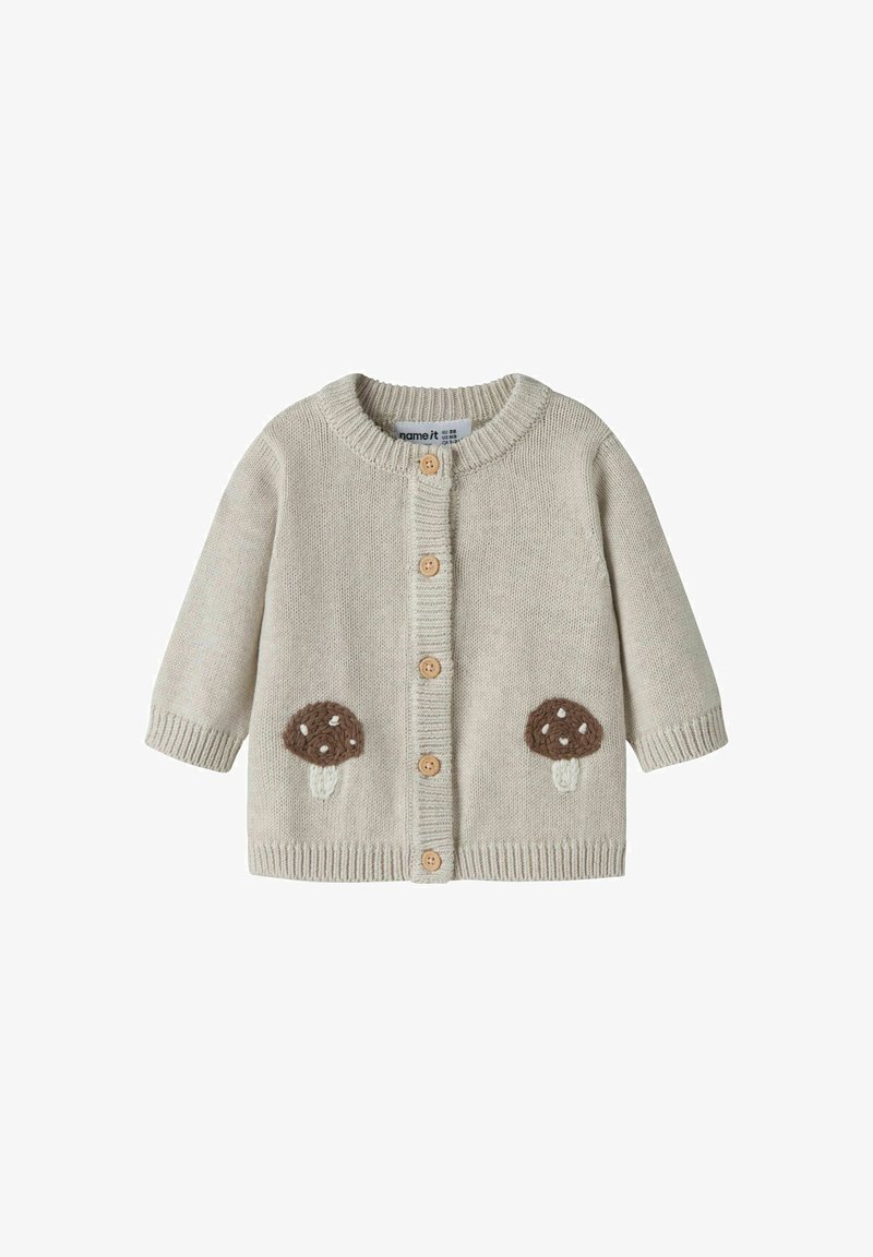 Cardigan bébé beige en maille avec col rond, boutons en bois sur le devant, et patches marron en forme de champignon de chaque côté près de l'ourlet.