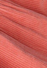 Zacht koraalroze corduroy stof met prominente verticale ribbels en vouwen die gemarmerde golven creëren.