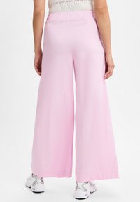 Lichtroze wijde broek met een soepele textuur en elastische tailleband, gecombineerd met witte en zilveren sportschoenen.