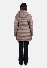 Cappotto imbottito di media lunghezza in taupe chiaro con cappuccio. Presenta cuciture orizzontali e un design aderente. Abbinato a jeans scuri e sneakers bianche.