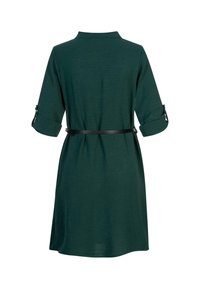 Dunkelgrünes Kleid mit Kragen, drei Viertel Ärmeln, die hochgerollt sind, und einem schwarzen Gürtel in der Taille. Glatter Stoff mit einer leichten Textur.