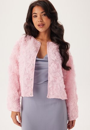 Roze cropped jas van bloemenstructuur stof met knoopsluiting. Draagt over een lichte paarse satijnen jurk, met gelaagde rozendetails.