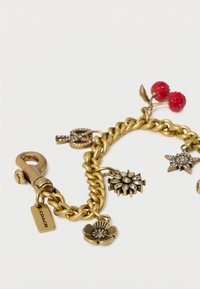 Kullatoonis käevõru lille-, tähe-, võtme- ja punase kirsi ripatsitega valgel taustal.