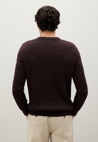 Maglione marrone scuro a coste con maniche a motivo a rombi texturizzati. Design aderente, collo a girocollo e dettagli del bordo a contrasto.
