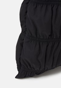 Czarna kurtka puchowa z marszczonym elastycznym wykończeniem, wykonana z gładkiego, błyszczącego materiału; miękka w dotyku i o wyraźnie zarysowanym kształcie.