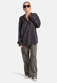 Camisa negra de botón con un corte relajado, combinada con pantalones de rayas de pierna ancha en negro y beige. Completado con zapatillas negras.