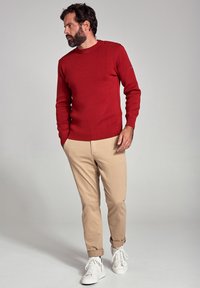Maglione rosso lavorato a maglia con scollo rotondo e bottoni laterali, abbinato a pantaloni beige chiaro e sneaker bianche, caratterizzato da una vestibilità rilassata.