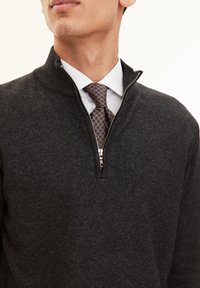 Dunkelgrauer Pullover mit einem Viertel-Reißverschluss, geripptem Kragen und glatter Textur. Eine gemusterte Krawatte in Brauntönen wird unter einem weißen Hemd getragen.