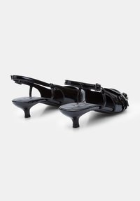 Fekete lakkbőr slingback sarkú cipők alacsony kúpos sarokkal, nyitott orral ésállítható csatpánttal. Simaság jellemzi őket fényes felülettel.