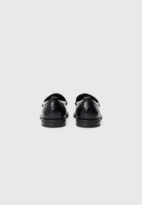Sorte lærersko med en glatt overflate, med en bakre stropp, rund tå og lav gummisåle. Minimalistisk design uten mønstre.