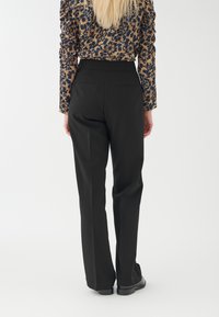 Schwarze, maßgeschneiderte Hose mit geradem Bein, ausgestattet mit seitlichen Taschen und einer glatten Textur, kombiniert mit einem gemusterten Oberteil.