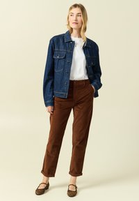 Jeansjacka i mörkblått, vit skjorta, bruna corduroybyxor och bruna ballerinas med leopardmönster. Jackan har knappar och fickor.