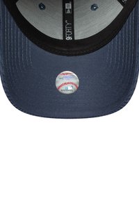 Spodnja stran temno modre bejzbolske kape z nalepko holograma MLB avtentičnosti na robu.
