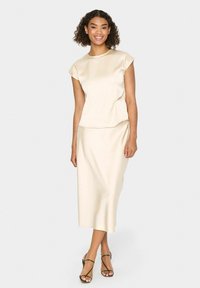 Beige Satin-Zweiteiler, bestehend aus einem kurzärmligen Oberteil mit rundem Ausschnitt und einem Midi-Rock. Glatte Textur und fließendes Design.