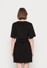 Vestito nero a maniche corte con scollo rotondo e dettagli arricciati sui lati. Realizzato in un tessuto morbido, ha una vestibilità leggermente ampia e arriva sopra il ginocchio.