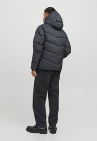 Pufferjakke i mørkegrå med hætte, med en quiltet design og elastiske cuffe, parret med sorte jeans og sorte støvler.