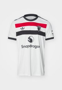 Valkoinen jalkapalloilupaita, jossa on punaisia ja mustia vaakaraitoja, musta kaulus ja brodeerattu vaakuna. Mukana on Snapdragon-logo.