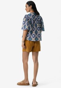 Haut à manches courtes à motifs en marine, bleu et moutarde, associé à un short moutarde. Le haut présente un design à dos froncé et des motifs géométriques.