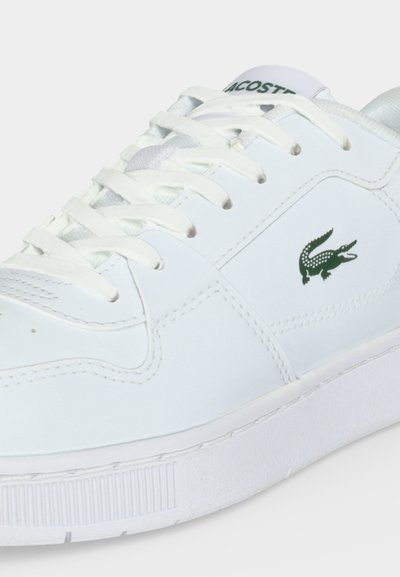 Бели кожени кецове с бели връзки и зелено лого на крокодил Lacoste отстрани и име на езика.