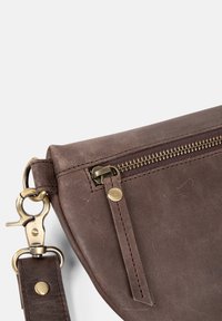 Hnědá kožená kabelka přes rameno s zipovým uzávěrem, mosaznými kovovými doplňky a odnímatelným popruhem. Obsahuje prošívané detaily a hladkou texturu.