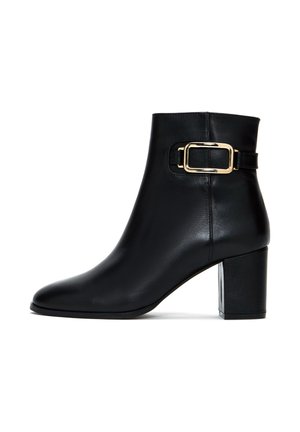 Black leather ankle boot with a rounded toe, block heel, and gold buckle detail on the strap. Smooth texture and sleek design.
