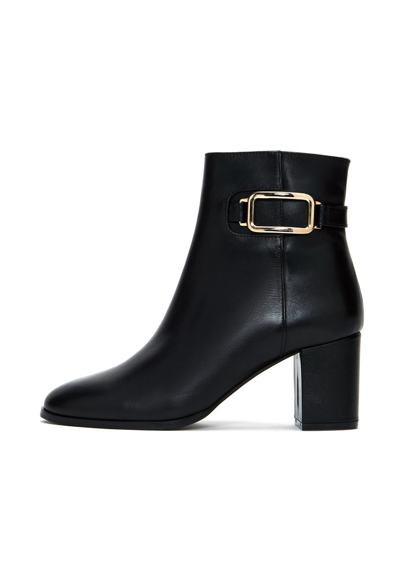 Bottine en cuir noir avec un bout arrondi, un talon carré et un détail de boucle dorée sur la sangle. Texture lisse et design épuré.