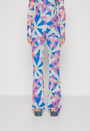 Full-length vibrant floral jumpsuit with blue, pink, white, and yellow petals, paired with blue platform sandals on a neutral background.