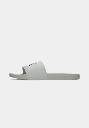 Grijze Calvin Klein slidesandaal met brede band met blauw "CK" logo, platte zool en reliëfbranding op de zijkant.