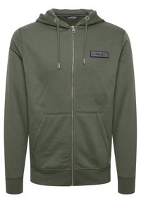 Grøn zip-up hoodie med en lomme foran, snøre i hætten, struktureret stof og et syet patch-label på brystet.