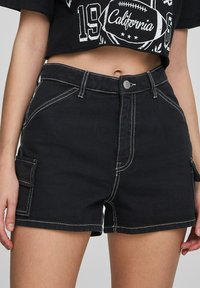 Shorts cargo neri con cuciture bianche, dotati di tasche laterali e design aderente. Realizzati in materiale resistente con una texture liscia.