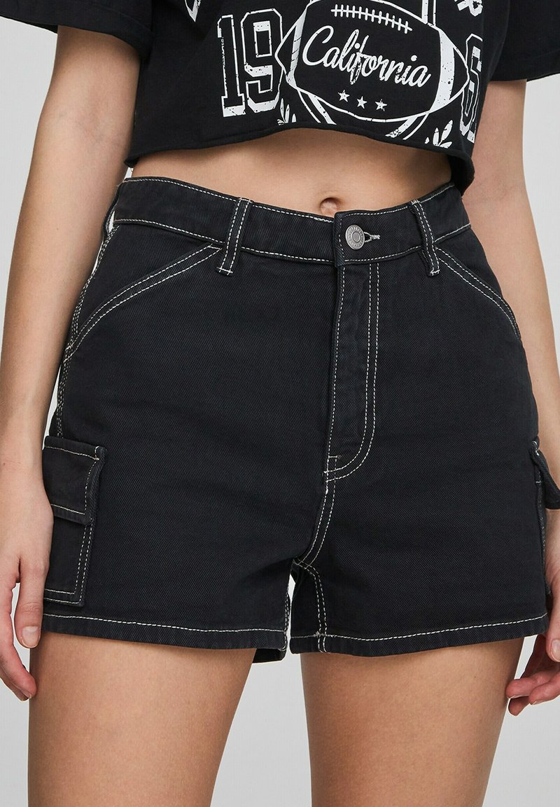Shorts cargo neri con cuciture bianche, dotati di tasche laterali e design aderente. Realizzati in materiale resistente con una texture liscia.