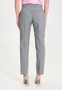 Pantaloni grigi a righe sottili con una vestibilità su misura, dotati di tasche laterali e una tasca posteriore, abbinati a tacchi alti color nude.