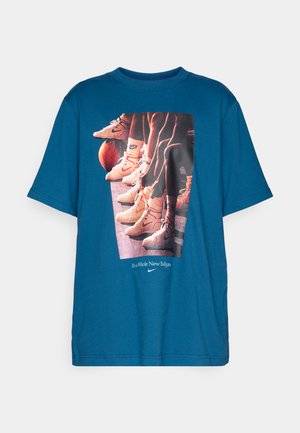 Teal t-shirt med grafik af basketballsko og ben opstillet ved siden af en basketball, med teksten "Det er et helt nyt spil" og Nike-logo.