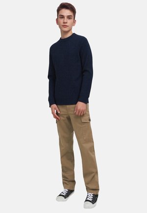 Navy knitted sweater with a textured pattern, beige cargo pants with side pockets, and black sneakers with white soles.
