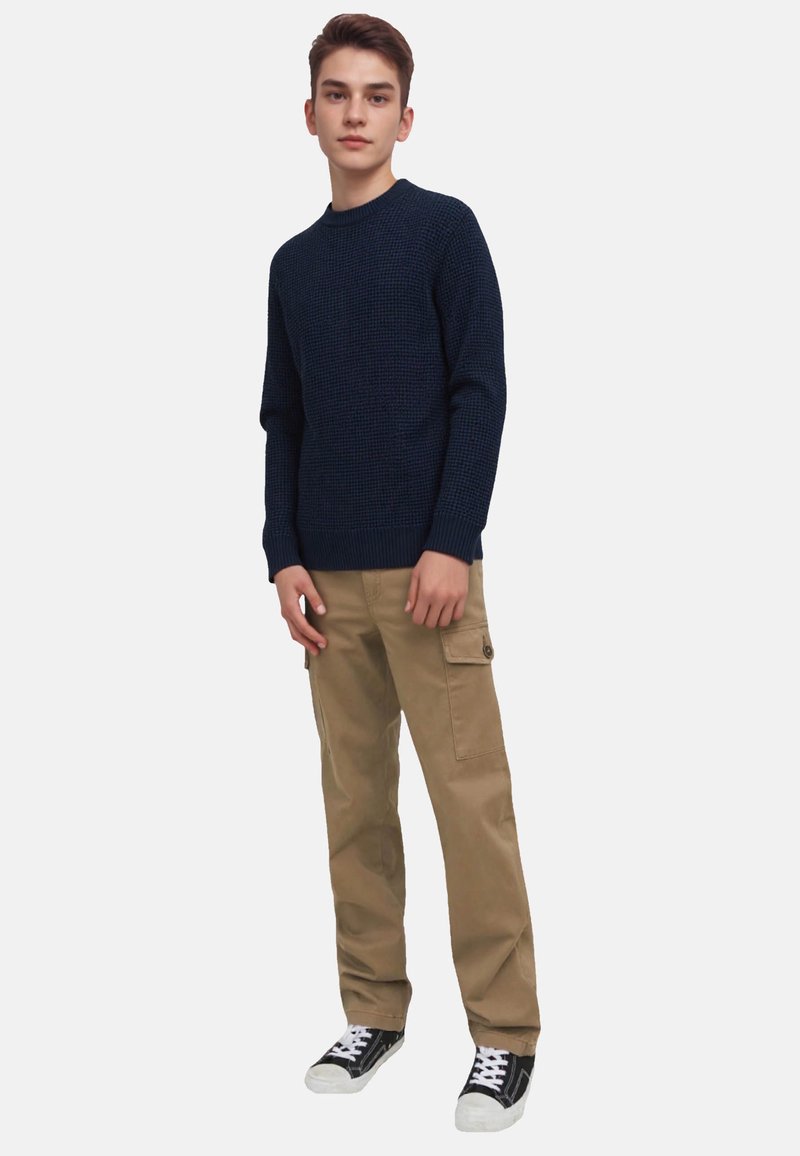Navy knitted sweater with a textured pattern, beige cargo pants with side pockets, and black sneakers with white soles.