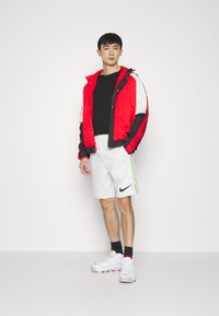 Giacca a vento rossa e nera con dettagli bianchi, pantaloni sportivi bianchi corti e scarpe da ginnastica bianche con dettagli rossi. Design semplice e atletico.