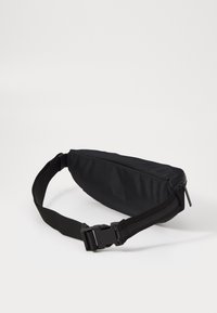 Zwarte nylon heuptas met een slanke, rechthoekige vorm, verstelbare band, ritssluiting en kunststof gesp. Gestructureerd oppervlak voor grip.