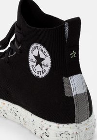 Černé pletené tenisky s vysokým střihem, které mají bílé hvězdné logo, texturovaný límec, bílou skvrnitou podrážku a šedé boční akcenty.