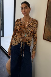 Animal print blouse in tan and black, featuring a tie-front design and long sleeves. Paired with high-waisted dark denim wide-leg pants.