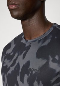 T-shirt de sport gris foncé présentant un motif abstrait subtil, un design à col ras du cou et un logo imprimé avec la mention "BORG" près de l'ourlet.