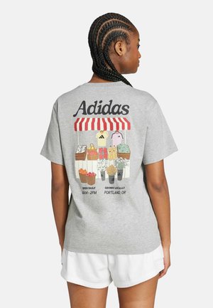 Camiseta gris de manga corta con un gráfico colorido de un mercado que incluye frutas y verduras, texto "Adidas" y un detalle de toldo a rayas rojas en la parte posterior.