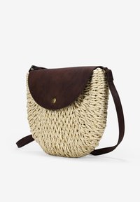 Bolso cruzado de paja trenzada con una tapa de cuero marrón, forma redonda y cierre de botón dorado. Correa ajustable para un transporte fácil.