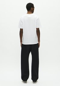 White short-sleeve t-shirt with a round neckline, paired with loose-fitting black trousers, shown from the back against a plain background.